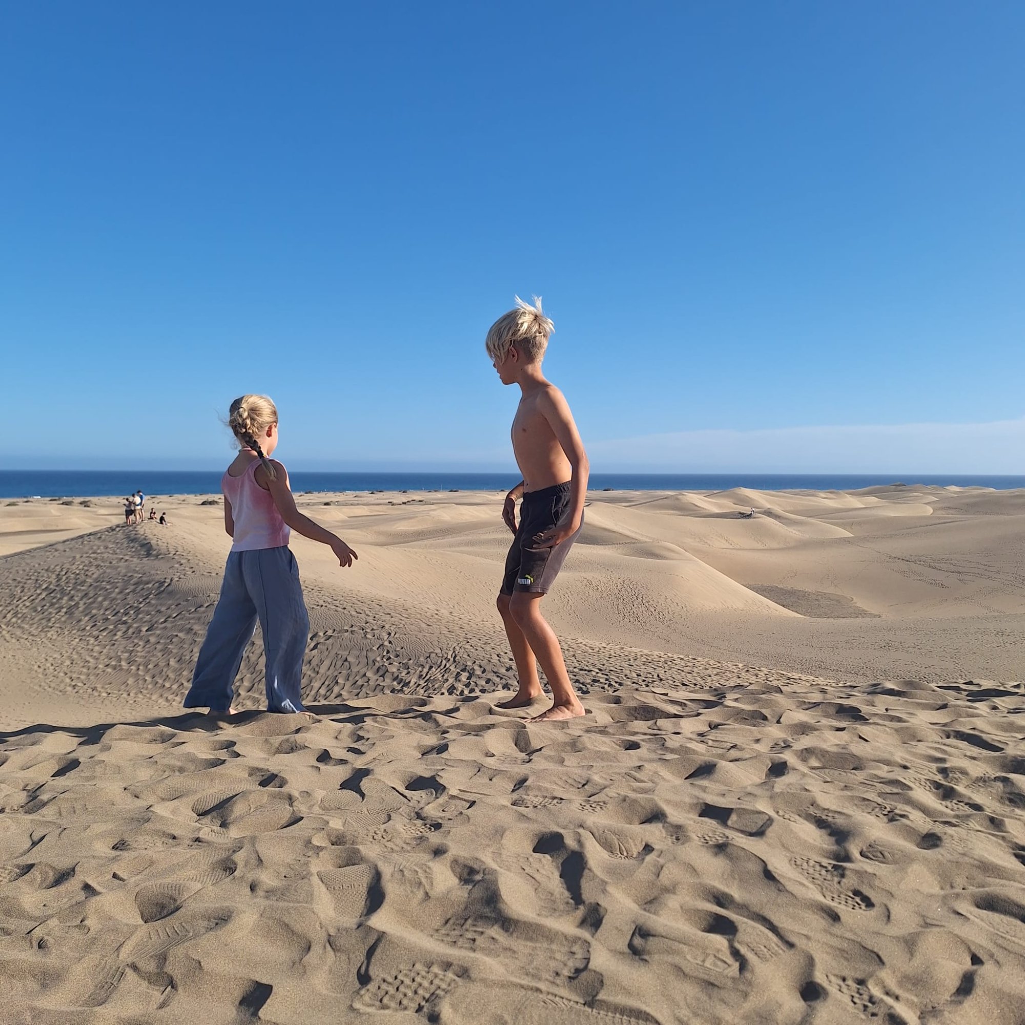 Two children exploring the sand dunes together with the Atlantic Ocean behind them