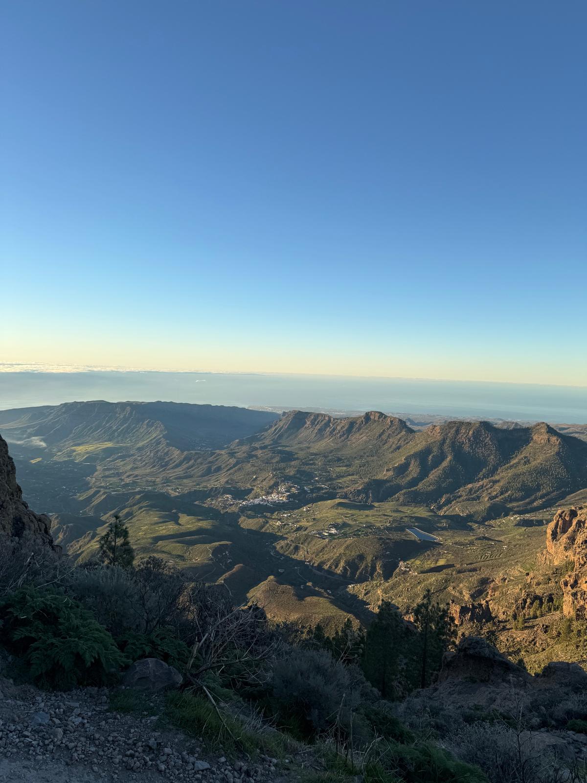 Panoramic sunrise view from Pico de las Nieves looking down across green valleys, villages, and the ocean in the distance