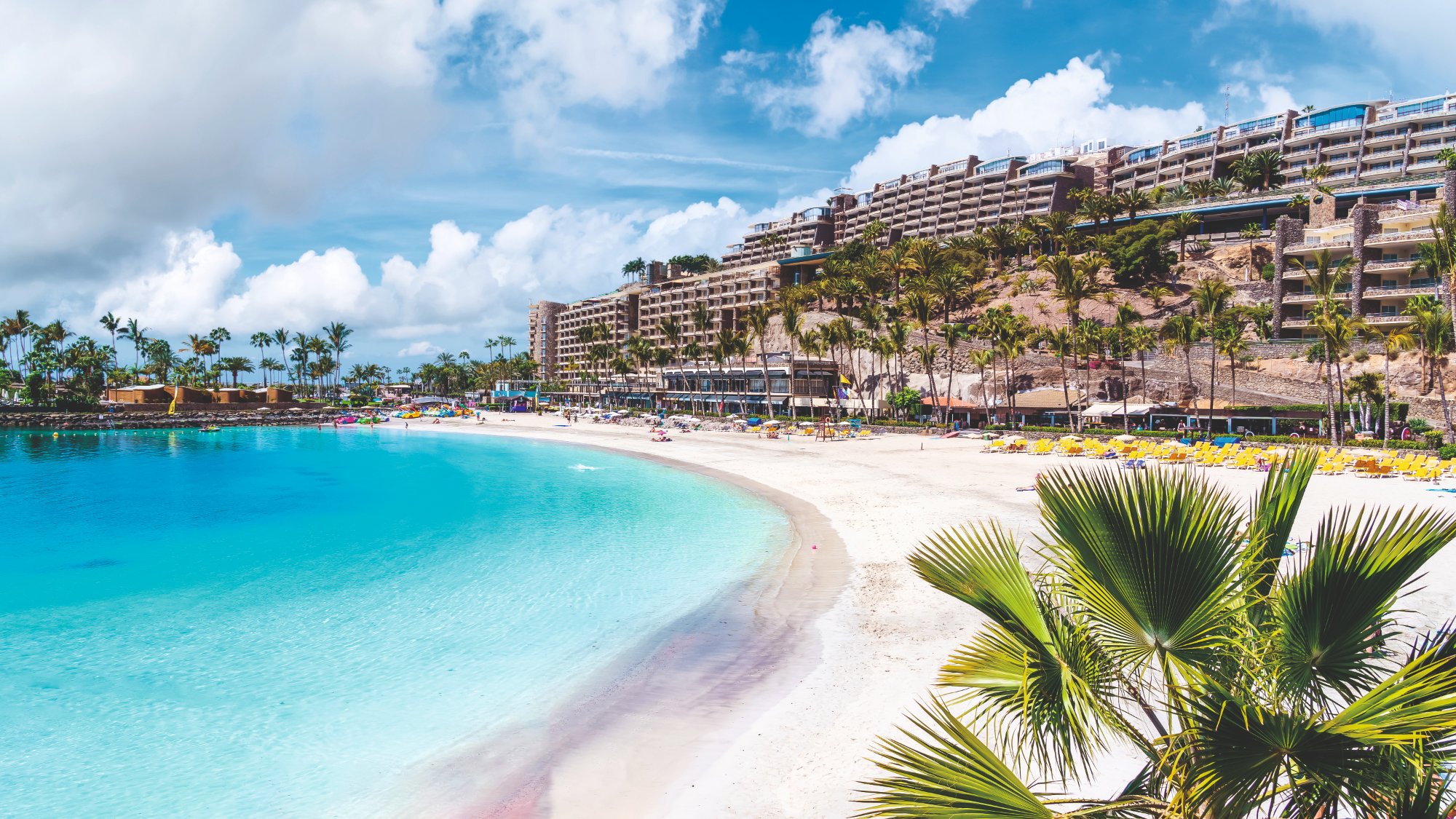 White sand and crystal turquoise water at Anfi del Mar beach with palm trees