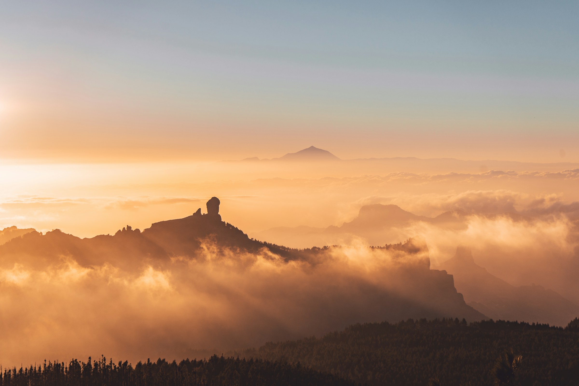 Roque Nublo silhouette at sunset with Tenerife visible through clouds on the horizon