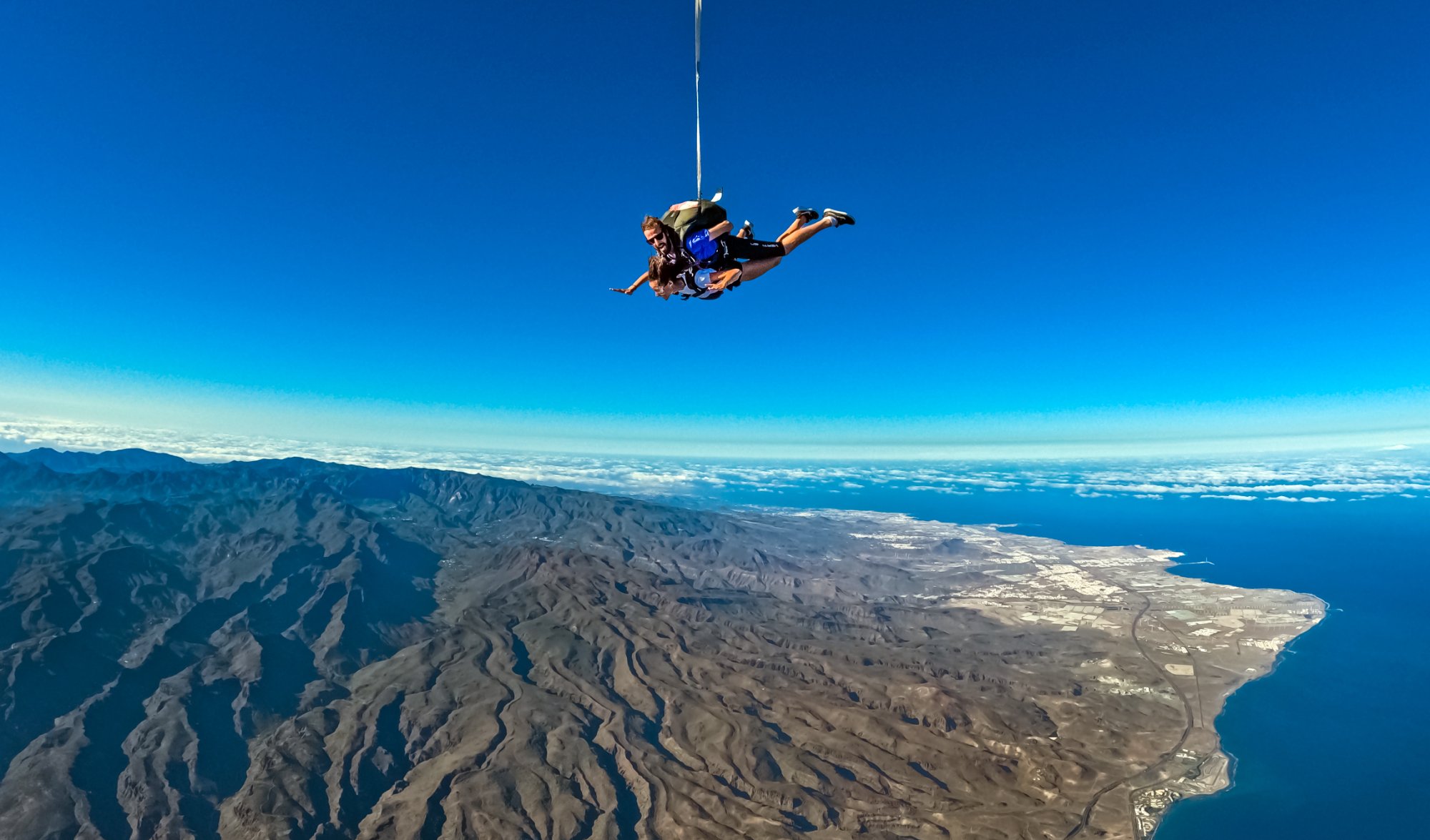 Tandem skydivers in freefall with breathtaking aerial view of Gran Canaria