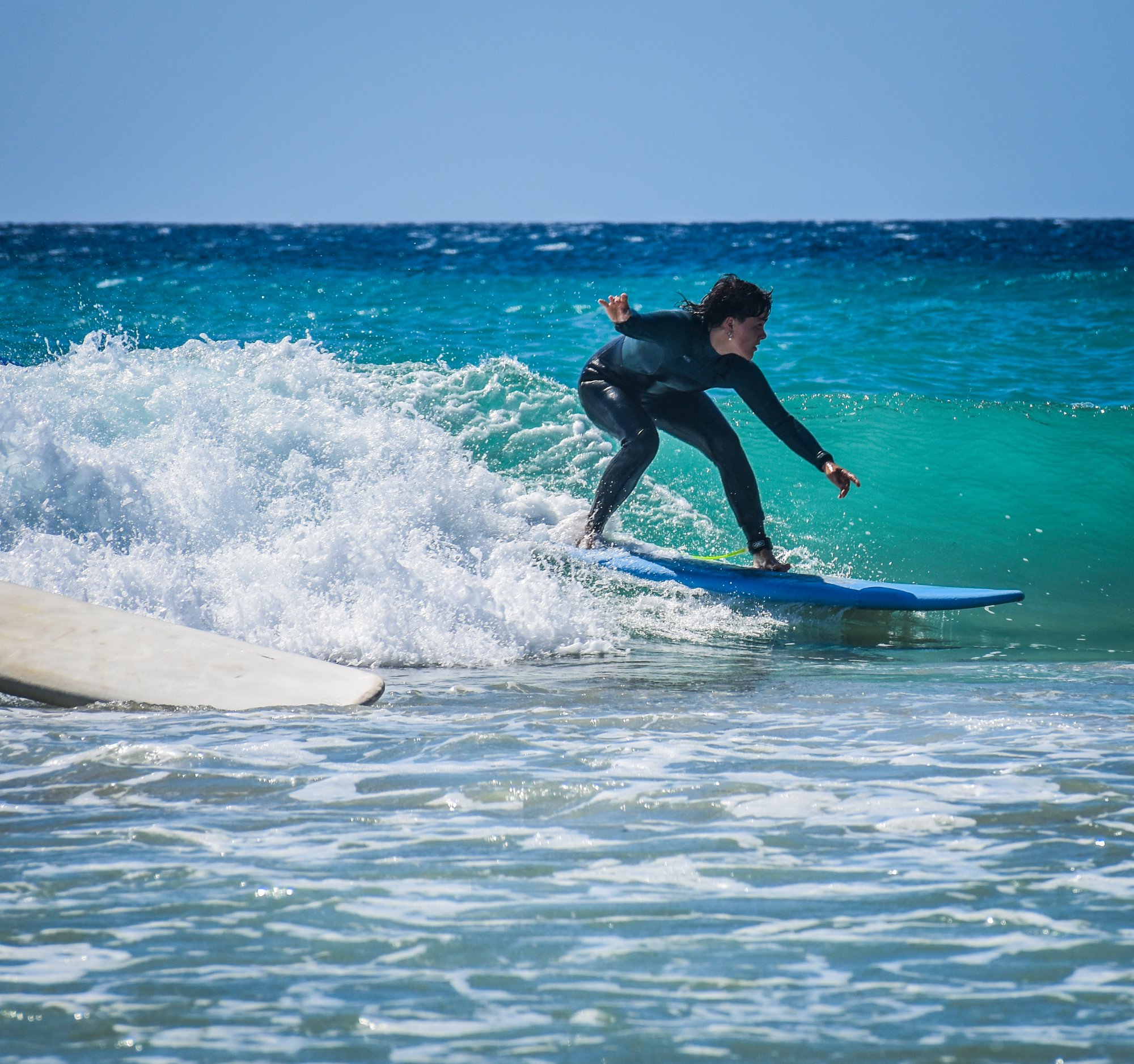 Young surfer riding a wave on a blue surfboard in turquoise Canarian waters